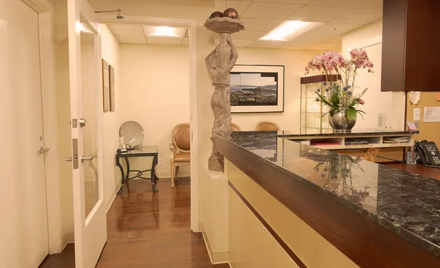 Reception area with a dark countertop and carved statue; a hallway with seating is visible.