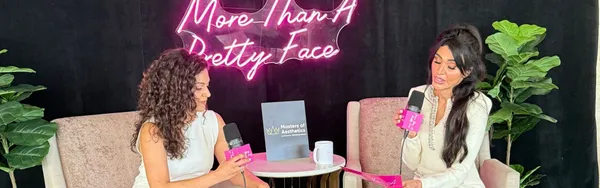 Two people sitting in armchairs during a podcast recording, with a neon sign.