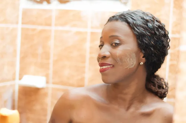 A woman is taking a shower and looking at her face in the mirror.